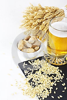 Glass of cold beer with chips and peanuts on white background