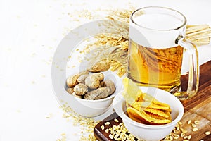 Glass of cold beer with chips and peanuts on white background