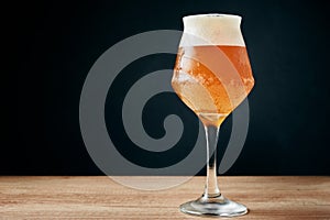 Glass of cold beer with foam on dark background