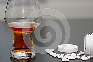 Glass of cold beer and headache pills on a gray surface - alcohol addiction concept