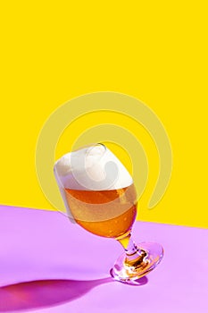 A glass of cold beer is placed on a vibrant yellow and purple background.