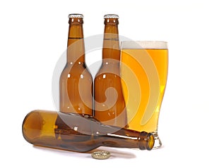 Glass of cold beer with several brown lager pils bottles isolated on white background