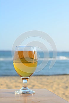 Glass of cold beer on wooden table at beach