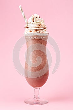 Glass of cold chocolate milkshake with whipped cream on pink background