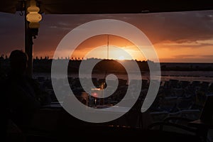 A glass of cold cocktail at the sunset on the table of a beach restaurant bar at the sunset, with blurry view on the beach and bay