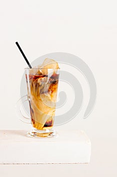 Glass of cold coffee or tea with milk and ice cubes on the white