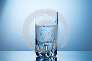 Glass of cold fresh sparkling mineral water on blue grandient background.
