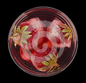 Glass with a cold red drink and with strawberries in ice cubes isolated on a black background