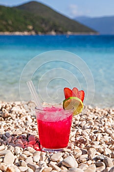 Glass of cold strawberry-daiquiri cocktail on the backgrond of Antisamos beach, Kefalonia island, Greece.