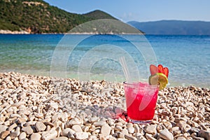 Glass of cold strawberry-daiquiri cocktail on the backgrond of Antisamos beach, Kefalonia island, Greece.