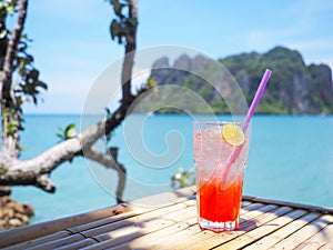 Glass of cold strawberry soda juice  on bamboo table over blue sea background
