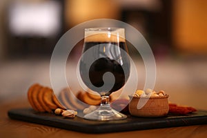 Glass of cold tasty dark beer served with snack on table