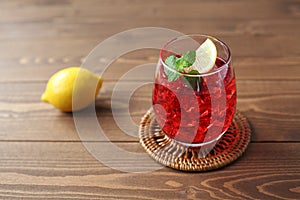 glass of cold tea red drink with lemon isolated on wooden table