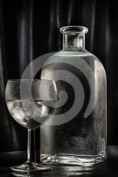 A glass of cold vodka or alcohol on the background of a beautiful bottle with drops. dark minimalistic still life
