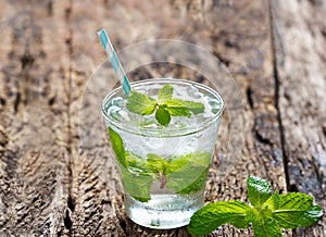 Glass of cold water with fresh mint leaves and ice cubes on old wooden background