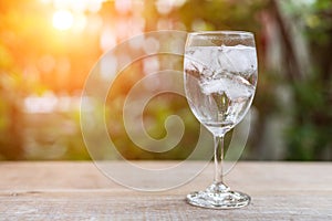 Glass of cold water with ice on table with blur nature garden ba