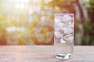 Glass of cold water with ice on table with blur nature garden