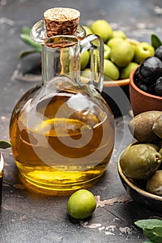 Glass container with olive oil branches and olives on a dark background. vertical image. top view. place for text