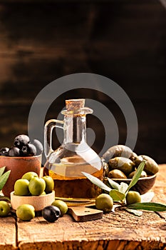 Glass container with olive oil branches and olives on a dark background. vertical image. top view. place for text