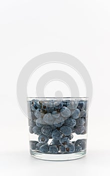 glass container with water and fresh blueberries against white background