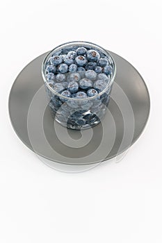 glass container with water and fresh blueberries on a gray plate against white background