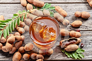 Glass of cool refreshing tamarind drink and some tamarind fruit on wooden table