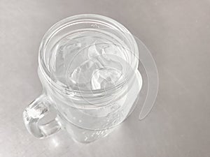 Glass of cool water with cube ice on gray table.