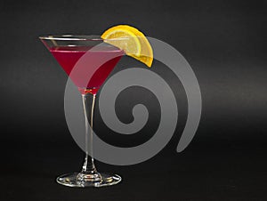 A glass of cosmopolitan cocktail decorated with slices of lemon and orange on black background.