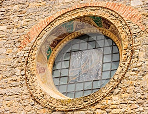 A Glass-covered 14th century fresco and rose window of the Charming Gothic Church of Saint George Chiesa di San Giorgio, Varenna