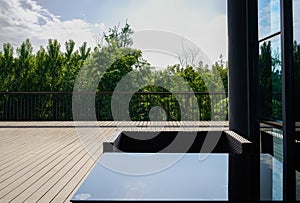 Glass-covered table and armchair on planked terrace in sunny sum