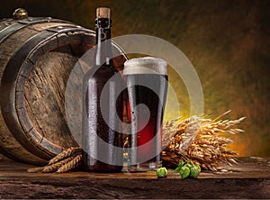 Glass of craft black beer, beer bottle and wooden cask on the wooden table in the cellar