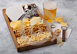 Glass of craft lager beer and opener with box of snacks on light background. Pretzel and crisps and salty potato sticks in vintage