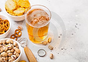 Glass of craft lager beer with snack and opener on stone kitchen table background. Pretzel and crisps and pistachio in white