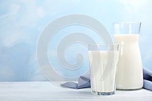 Glass and cruet with fresh milk on table against color background