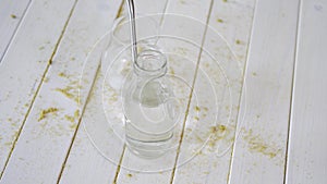 Glass of crystal water with titanium straw and bottle on wooden table with sand
