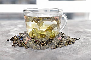 Glass cup of aromatic green tea and dry leaves on table