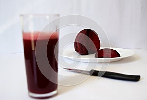 Glass cup with beetroot and beetroot juice on white plate with knife