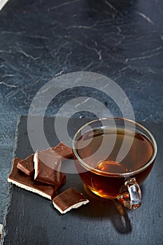 A glass cup of black tea with chocolate on a dark greyish marble background, shallow depth of field. Breakfast