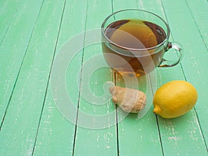 Glass cup of black tea, lemon and ginger on a mint-colored wooden table