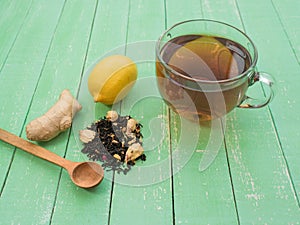 Glass cup of black tea, lemon and ginger on a mint-colored wooden table