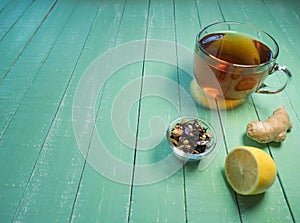 Glass cup of black tea, lemon and ginger on a mint-colored wooden table