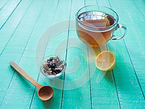 Glass cup of black tea and lemon on a mint-colored wooden table