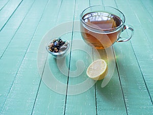 Glass cup of black tea and lemon on a mint-colored wooden table