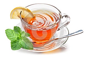 Glass cup with black tea, a slice of lemon and mint leaves isolated on a white background