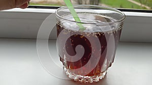 Glass cup with brown sparkling cocktail drink and green straw