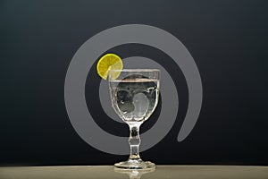 a glass cup with clear water and a lemon on the rim. Isolated on gray background