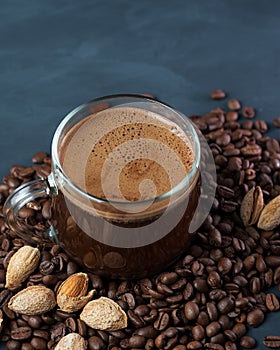 A glass Cup of coffee with grated roasted almonds on a concrete table and scattered roasted grains