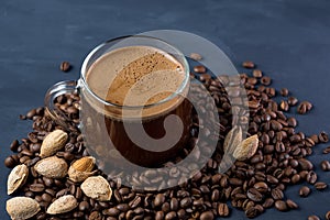 A glass Cup of coffee with grated roasted almonds on a concrete table and scattered roasted grains