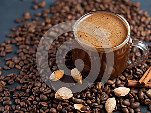 A glass Cup of coffee with grated roasted almonds on a concrete table and scattered roasted grains
