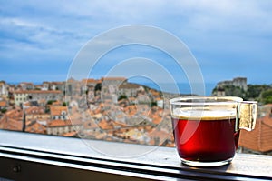 Glass cup of coffee or tea on balcony with view on Dubrovnik city center. View from above of red rooftops, historic old town and